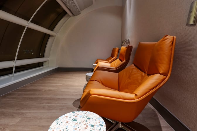 Reclining chairs in The Club MCO Airside 4 lounge offer comfortable seating with views of the airport through large windows.