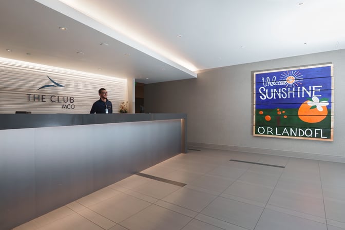 The Club MCO reception area features a staffed front desk and a welcoming sign for Orlando, located airside at Orlando International Airport.