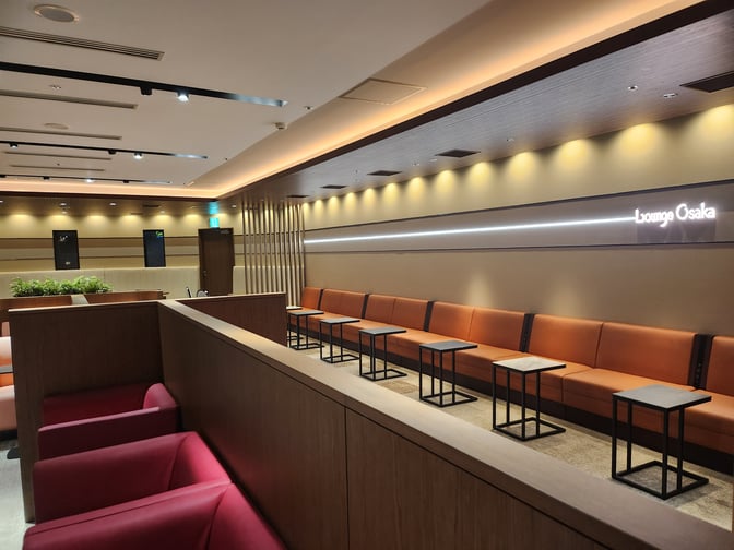 Seating area in Lounge Osaka at Osaka-Itami Airport features rows of cushioned benches and small tables for travelers.