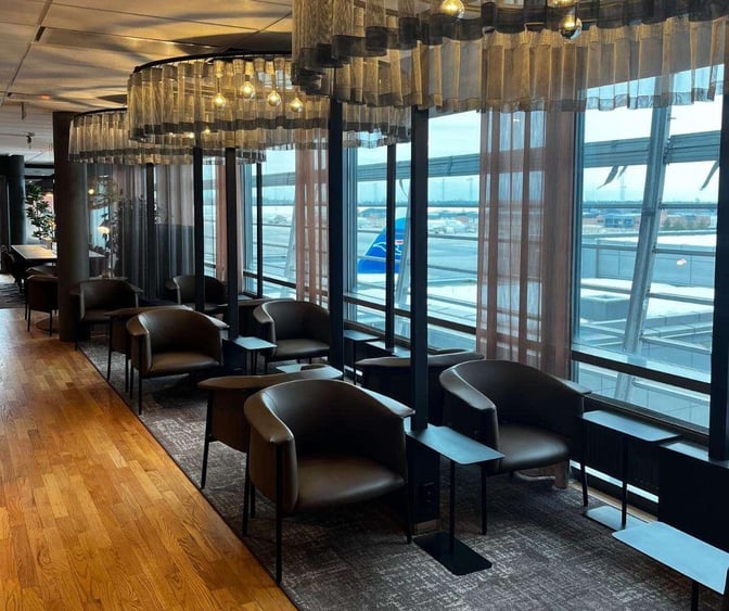 Seating area at OSL Lounge International features individual chairs with side tables, offering views of the airport through large windows.