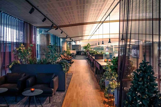The OSL Lounge Innland at Oslo Airport features a seating area with armchairs, tables, and greenery, offering a relaxing environment.