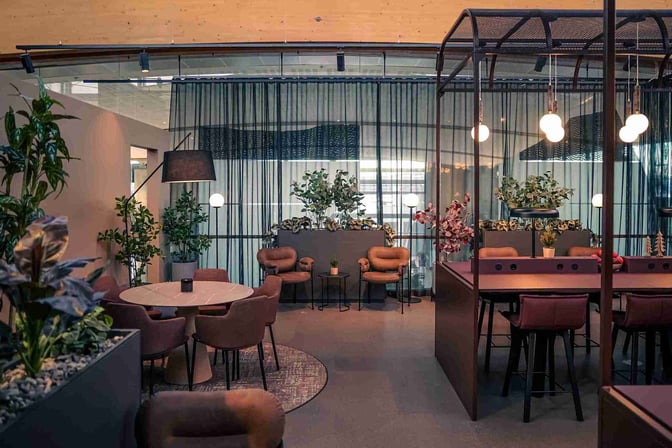 The OSL Lounge Innland at Oslo Airport features seating areas with round tables, armchairs, and workstations surrounded by plants.