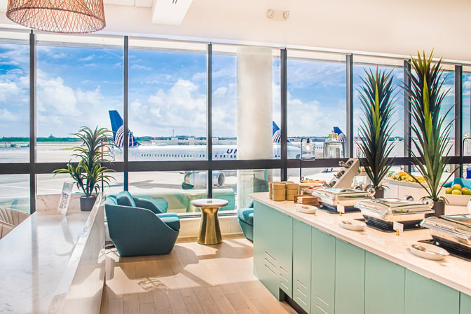 The Escape Lounge at Palm Beach International Airport features a self-serve food area with runway views through large windows.