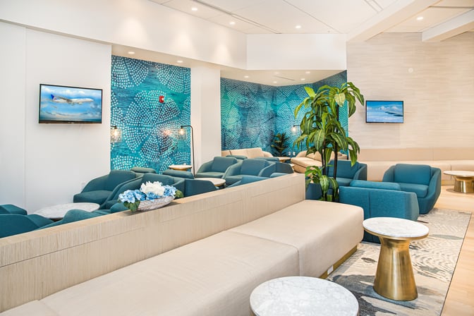 The seating area in the Escape Lounge at Palm Beach International Airport features comfortable chairs, small tables, and wall-mounted televisions.