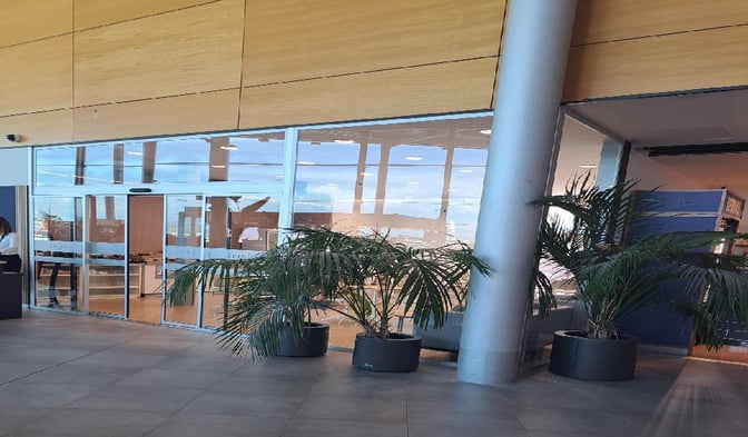 The entrance to the Mestral VIP Lounge at Palma de Mallorca Airport features glass doors and potted plants, located in the terminal area.