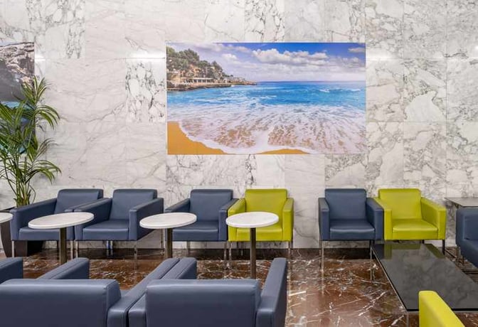 Seating area in Sala VIP Llevant at Palma de Mallorca Airport features individual chairs and small tables with a beach-themed wall art.