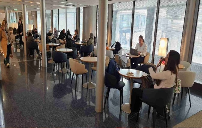 The seating area in Salon Paris at Charles de Gaulle Airport features round tables and chairs, accommodating travelers with laptops and refreshments.