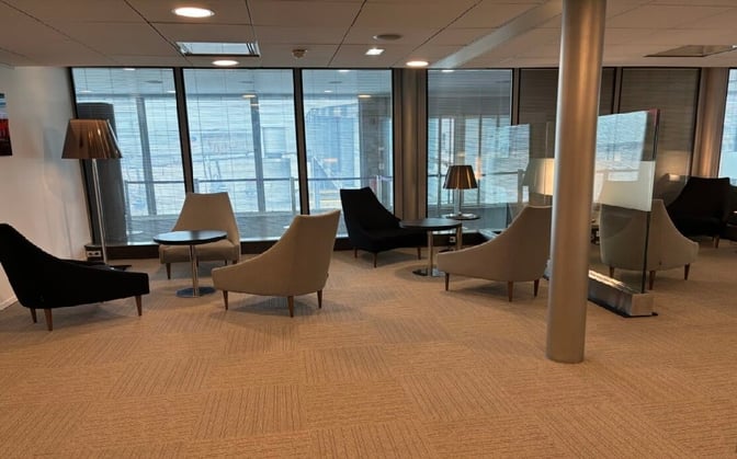 The seating area in Salon Paris at Charles de Gaulle Airport features armchairs and tables with views of the tarmac through large windows.