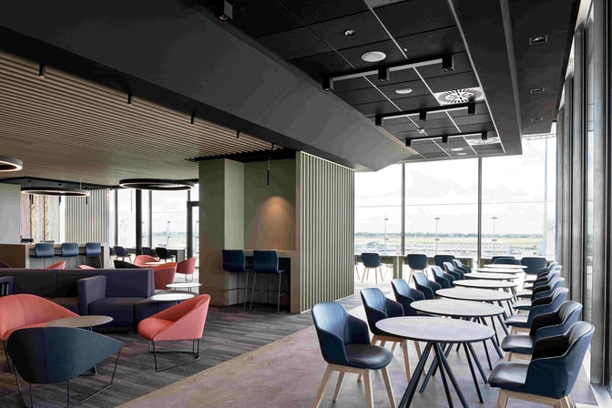 The Primeclass Lounge at Paris-Orly Airport features a seating area with various chairs and tables, offering views of the tarmac.