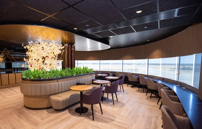 The seating area in the International Aspire Lounge at Perth Airport features tables, chairs, and window views of the airfield.