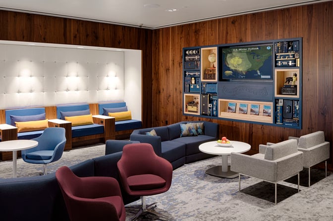The seating area in the Escape Lounge at Phoenix Sky Harbor offers various chairs and sofas with a display wall featuring travel-themed decor.