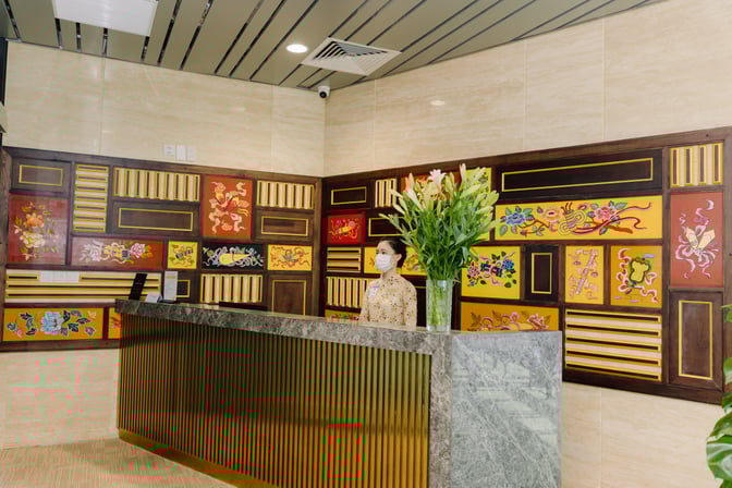 The reception area of SH Premium Lounge Phu Bai features a decorative wall and a staffed counter with floral arrangements.