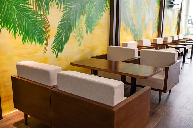Seating area in SH Premium Lounge Phu Cat features cushioned chairs and wooden tables against a wall with palm leaf artwork.