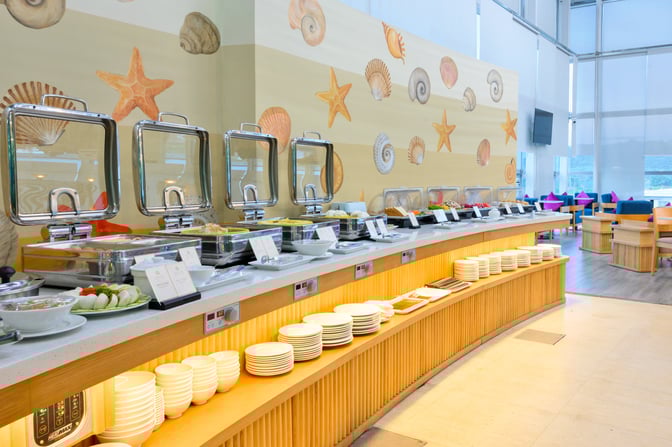The buffet area at SH Premium Lounge Phu Quoc 1 offers a variety of hot and cold dishes with ample seating nearby.