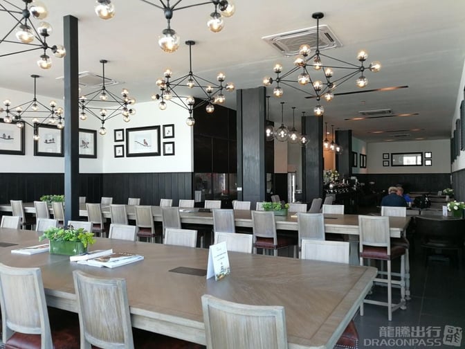 The Coral Premium Departure Lounge at Phuket International Airport features communal dining tables and framed artwork, providing a spacious seating area.