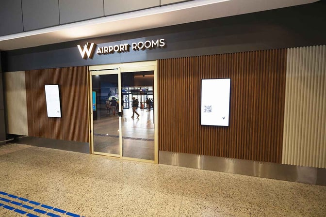 The entrance to W Airport Rooms at Fortaleza International Airport features sliding glass doors and digital information displays on either side.