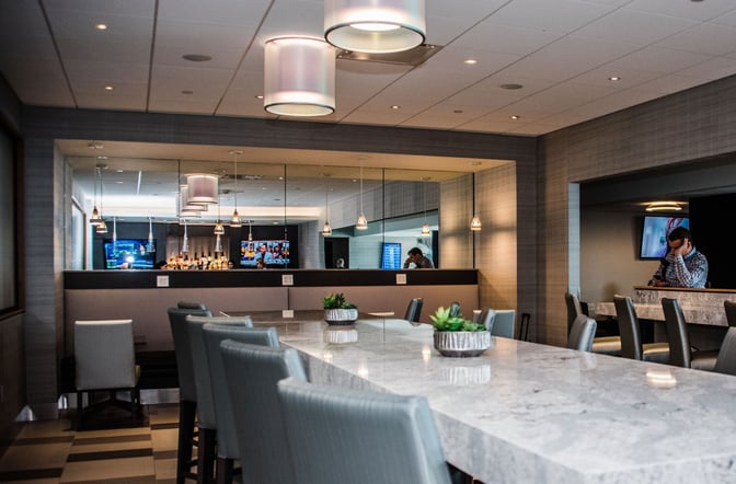 The Club PIT at Pittsburgh International Airport features a bar area with counter seating and televisions for entertainment.