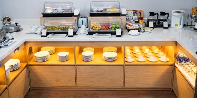 The SH Premium Lounge at Pleiku Airport features a self-serve food station with covered dishes, fresh fruit, and beverage options.