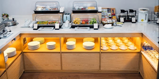 The SH Premium Lounge at Pleiku Airport features a self-serve food station with covered dishes, fresh fruit, and beverage options.