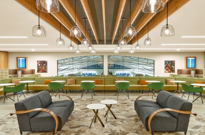 The seating area in the Escape Lounge at Portland International Airport features sofas, tables, and booth seating with airport views.