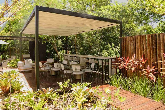 The outdoor seating area at BRT Lounge Porto Seguro features tables and chairs under a pergola, surrounded by lush greenery.