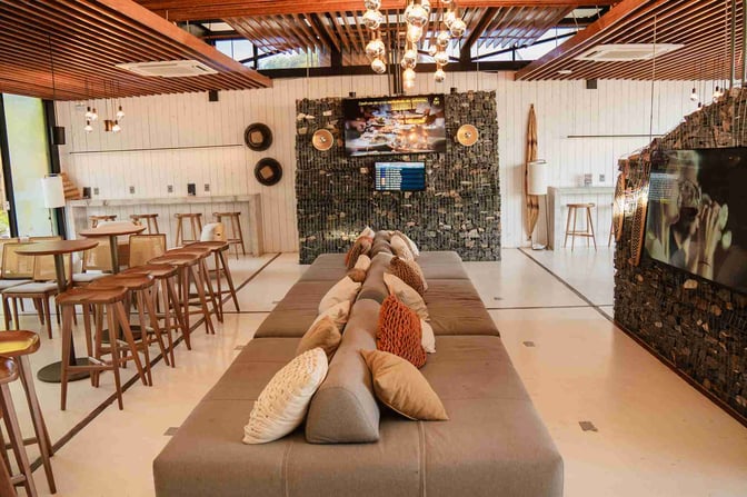 The BRT Lounge at Porto Seguro Airport features a seating area with cushioned benches, bar stools, and a wall-mounted screen.