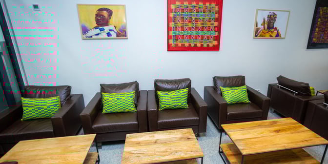 The seating area in the CIP Lounge at Prempeh I International Airport features comfortable armchairs and wooden tables with decorative artwork on the walls.