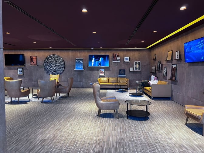 The Al Ula Lounge at Prince Abdul Majeed bin Abdulaziz Airport features comfortable seating with wall-mounted screens and decorative artwork.
