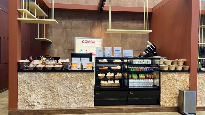 The food area at Al Ula Lounge features a self-serve station with snacks, beverages, and combo meal options for travelers.