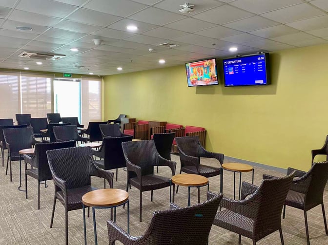 The seating area in PAGSS Lounge at Puerto Princesa International Airport features wicker chairs, small tables, and departure information screens.