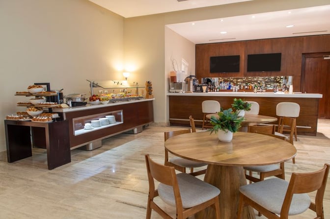 The Punta Cana International Airport VIP Lounge features a self-serve buffet with pastries and fruits, alongside a bar area with seating.