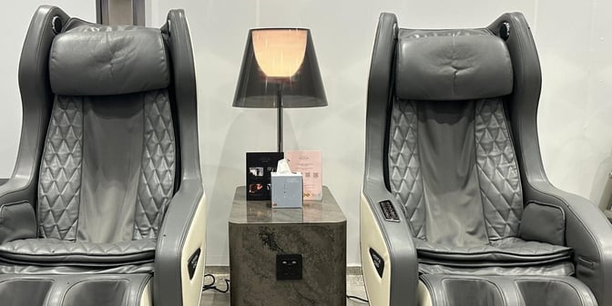 Two massage chairs in the Hayyak Lounge at Qaisumah–Hafar Al-Batin International Airport are positioned beside a small table with a lamp.