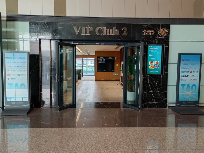 The entrance to VIP Club 2 at Qingdao Liuting International Airport features open doors and digital signage displaying airline partnerships.