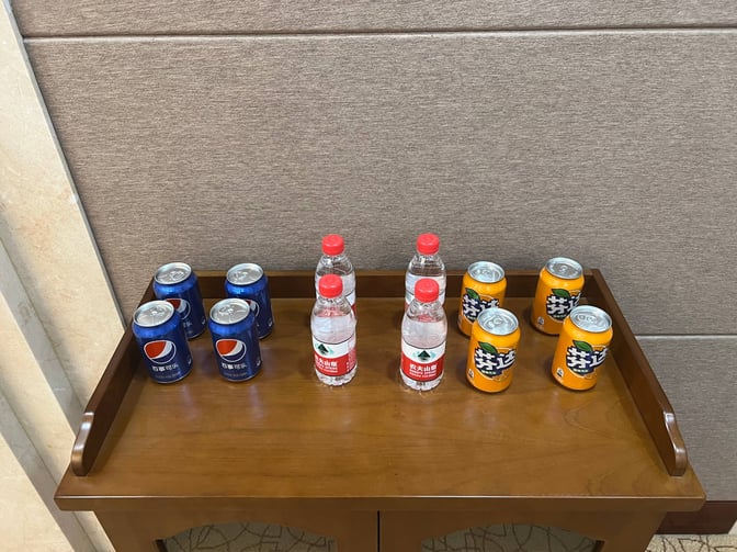 A selection of complimentary beverages, including bottled water and canned sodas, is available on a wooden table in the lounge.