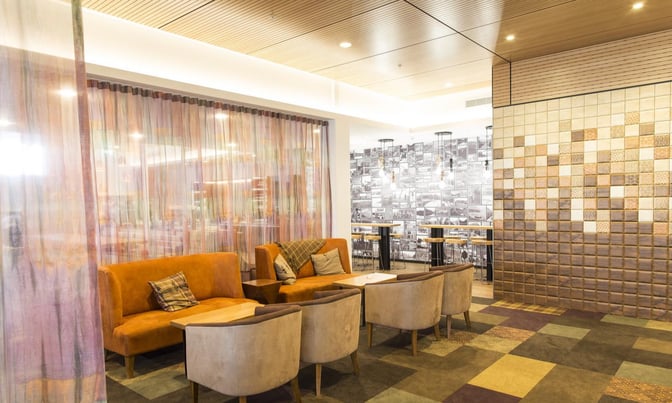 The Manaia Lounge at Queenstown Airport features a seating area with cushioned chairs and tables, adjacent to a tiled wall.