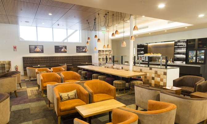 The Manaia Lounge at Queenstown Airport features a seating area with armchairs, tables, and a self-serve food station.