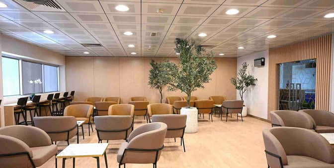 Seating area in Ras Al Khaimah International Airport lounge features armchairs and tables with additional counter seating by the window.