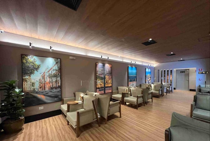 The seating area in W Premium Lounge Recife Sao Joao features comfortable chairs and wall art, providing a relaxing space for travelers.