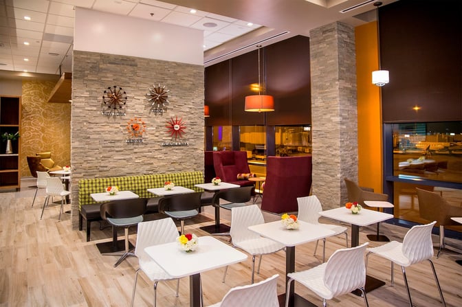 The seating area in the Escape Lounge at Reno–Tahoe International Airport features tables with chairs and booth seating near large windows.