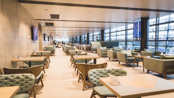 The Primeclass Business Lounge at Riga International Airport features spacious seating with tables and armchairs, offering views of the tarmac.