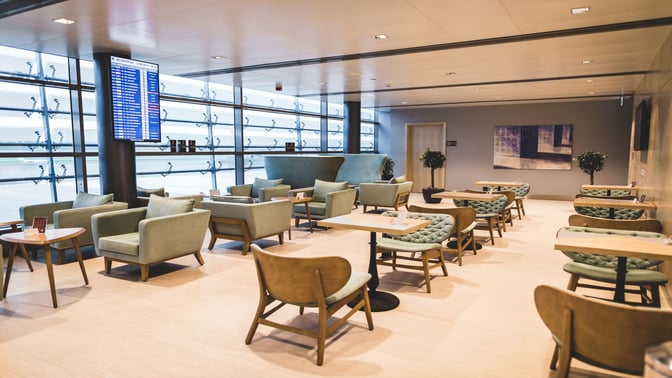 The seating area in the Primeclass Business Lounge at Riga International Airport features armchairs and tables with a view of the tarmac.