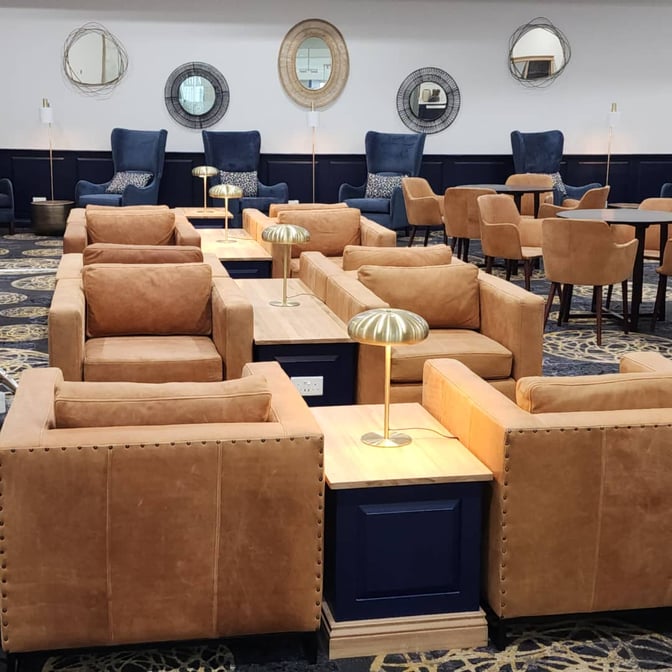 The seating area in Khami Lounge at Robert Mugabe International Airport features armchairs and tables with lamps for passenger comfort.