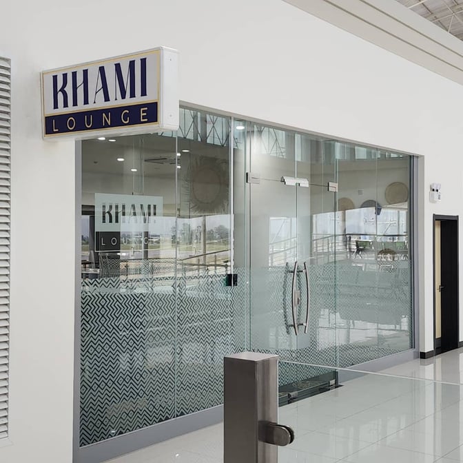 The Khami Lounge entrance at Robert Mugabe International Airport features glass doors with patterned panels and is located in the terminal area.