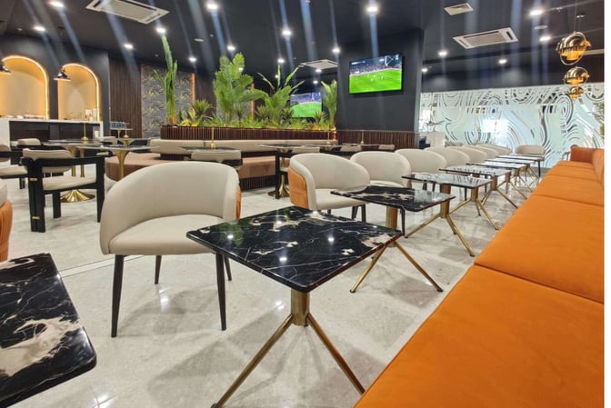 The seating area at Robert Mugabe International Airport lounge features tables, chairs, and a television for passenger relaxation and entertainment.