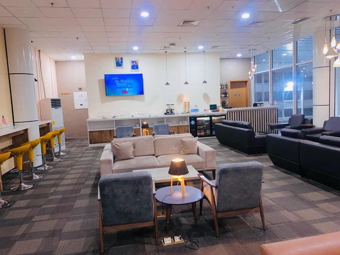 The Sanbra Business & Priority Lounge at Roberts International Airport features comfortable seating, a self-serve beverage area, and a television.