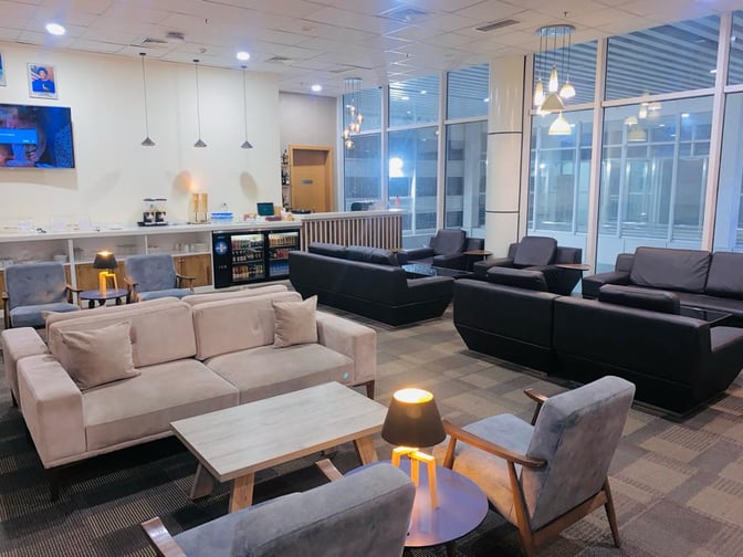 The Sanbra Business & Priority Lounge at Roberts International Airport features comfortable seating areas with sofas, armchairs, and a self-serve refreshment counter.