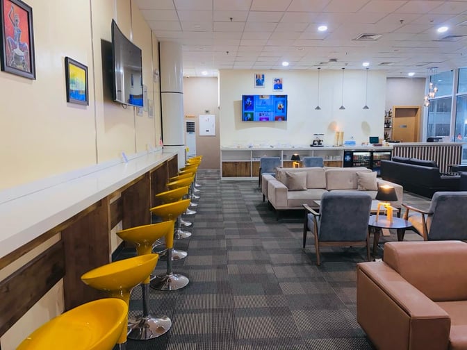 The Sanbra Business & Priority Lounge at Roberts International Airport features a seating area with couches, bar stools, and a television.
