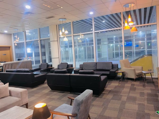 The Sanbra Business & Priority Lounge at Roberts International Airport features a seating area with sofas and armchairs near large windows.