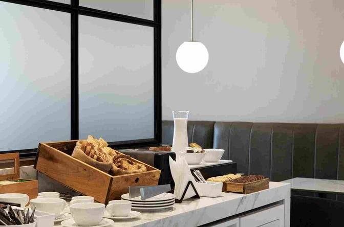 The AMAE Lounge at Rosario Airport features a self-serve breakfast station with breads, cookies, and beverages, alongside booth seating.