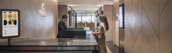 The reception area of Plaza Premium Lounge at Sabiha Gokcen International Airport features a check-in counter and digital information displays.